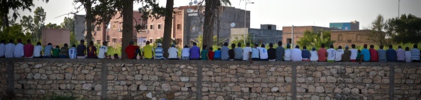 Guys hanging out watching soccer on the other side of the wall.
